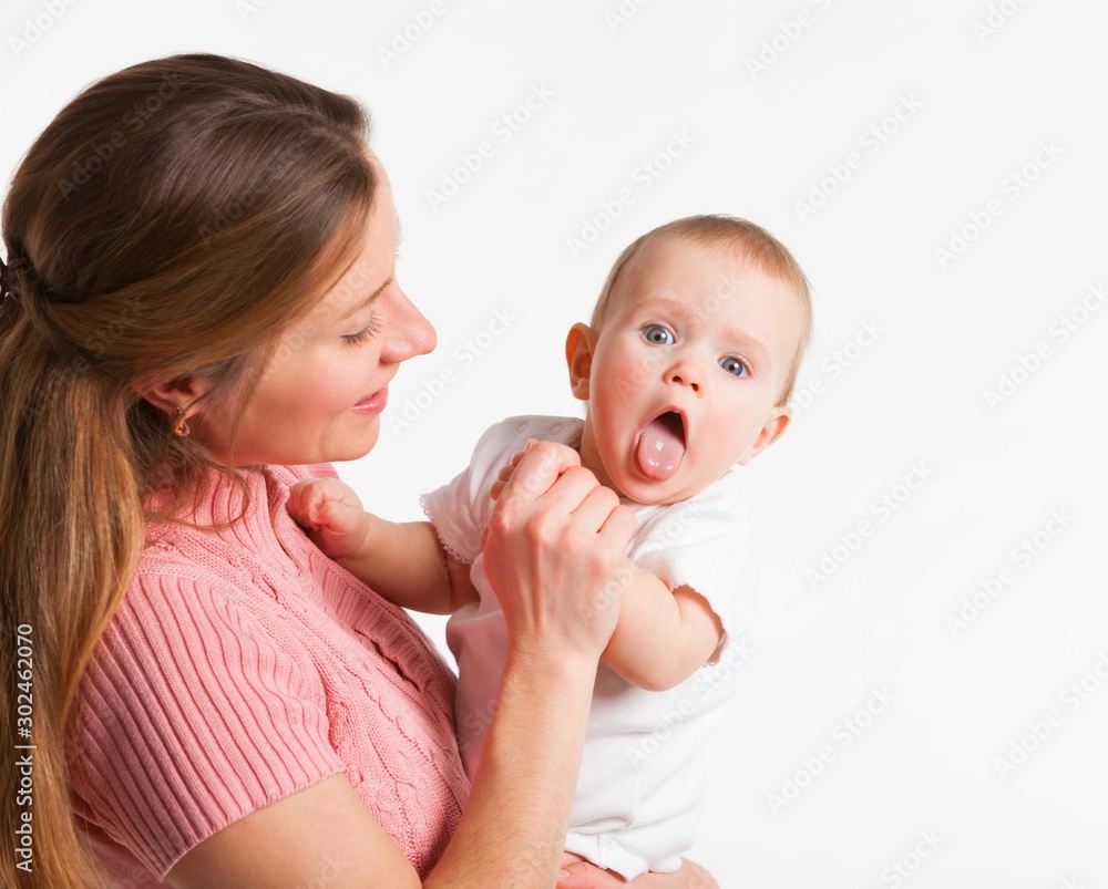 Positive young mother holds on her hands a charming little daughter showing tongue on a white background. Concept care for little newborn babies. Advertising space Positive young mother holds on her hands a charming little daughter showing tongue on a white background. Concept care for little newborn babies. Advertising space