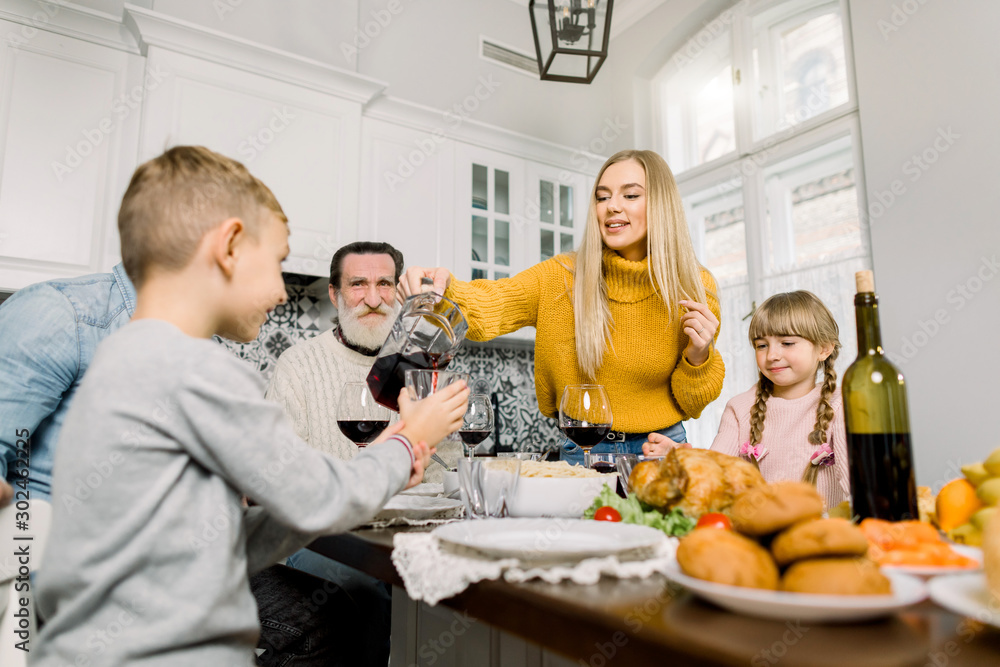 Pretty young mother pouring cherry juice for son at holiday dinner. happy large family having holiday dinner on thanksgiving day