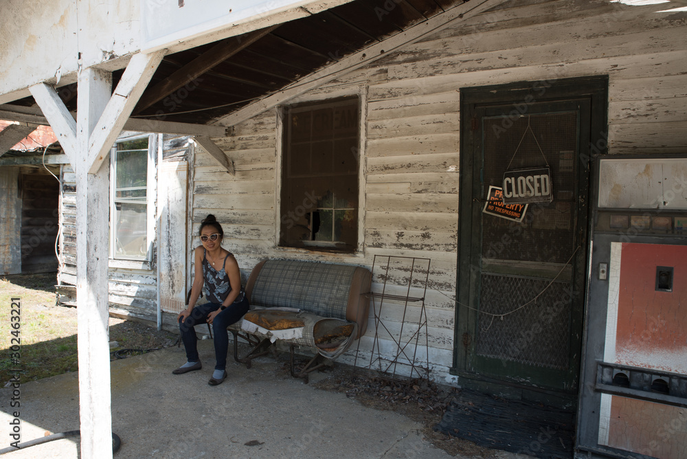 woman in sun glasses sitting on bench in abandoned gas station woman in sun glasses sitting on bench in abandoned gas station