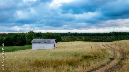 White barn in a field with sky and clouds in the background