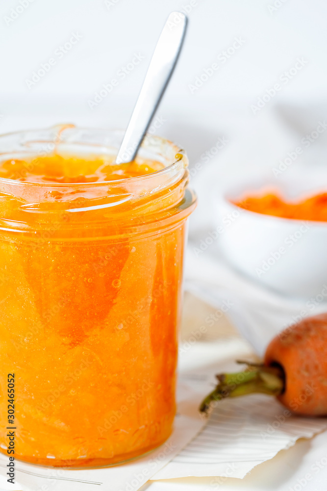 Vegetarian carrot jam or marmalade with orange juice in a glass jar on a white background close-up.Healthy organic vegetable dessert for breakfast.Vertical orientation Vegetarian carrot jam or marmalade with orange juice in a glass jar on a white background close-up.Healthy organic vegetable dessert for breakfast.Vertical orientation