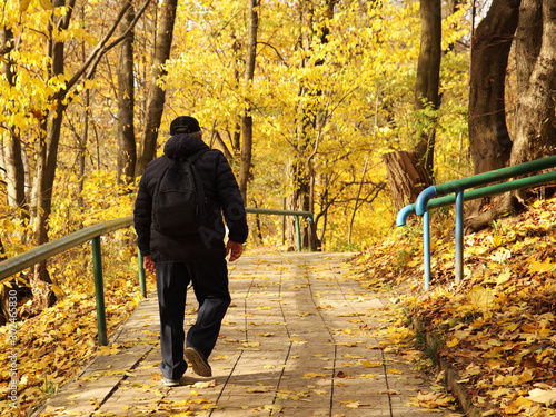 A man walks along an alley in an autumn park among yellow fallen leaves. Change of seasons. Wilting nature. An abundance of warm colors. Fiery colors. Walk in the fresh air in a festive atmosphere