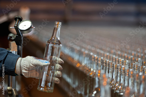 Glassworks. Glass industry. Working hands hold a glass bottle on the background of a conveyor belt.