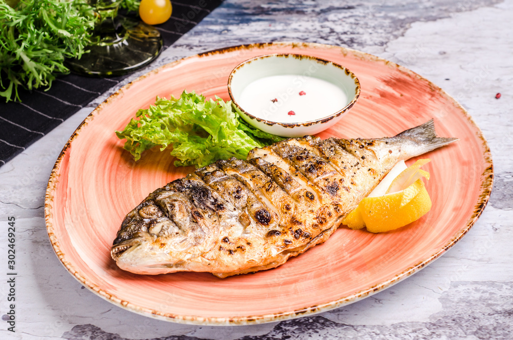 Restaurant food - whole grilled dorado with lemon slices and green beans on platter, restaurant table. Top view baked fish Restaurant food - whole grilled dorado with lemon slices and green beans on platter, restaurant table. Top view baked fish