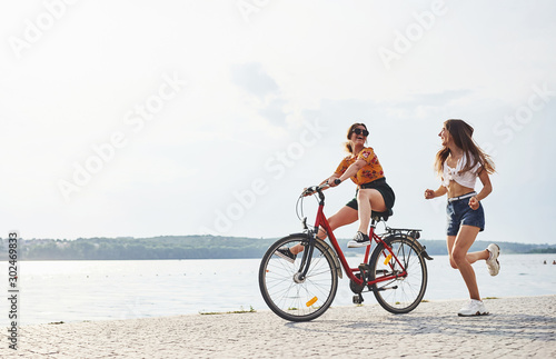 Girl runs near bicycle. Two female friends on the bike have fun at beach near the lake