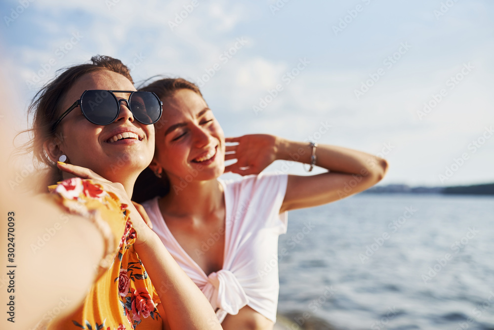 Selfie of two smiling girls outdoors that have a good weekend together at sunny day against the lake Selfie of two smiling girls outdoors that have a good weekend together at sunny day against the lake