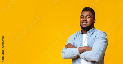 Attractive black guy with folded arms over yellow background
