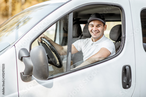 Slika na platnu Portrait of a cheerful delivery driver in uniform looking out the window of the