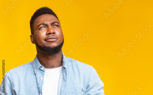 Фотография Portrait of suspicious black guy looking upwards at copy space