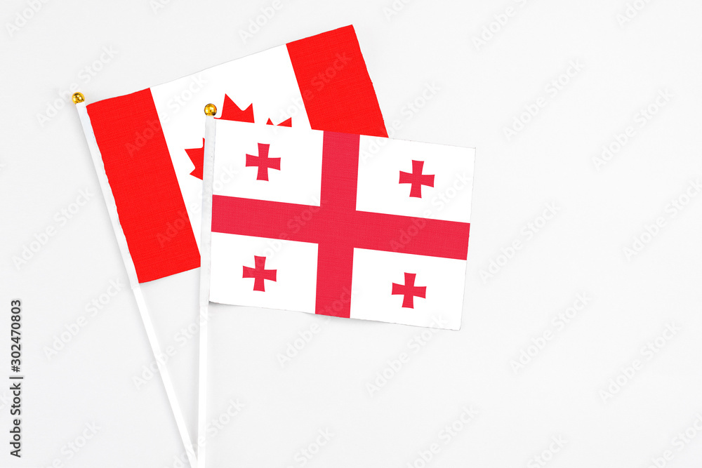 Georgia and Canada stick flags on white background. High quality fabric, miniature national flag. Peaceful global concept.White floor for copy space.