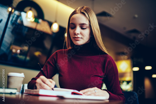 Foto Young pondering intelligent female student preparing for coursework project and making some notating during sitting indoors