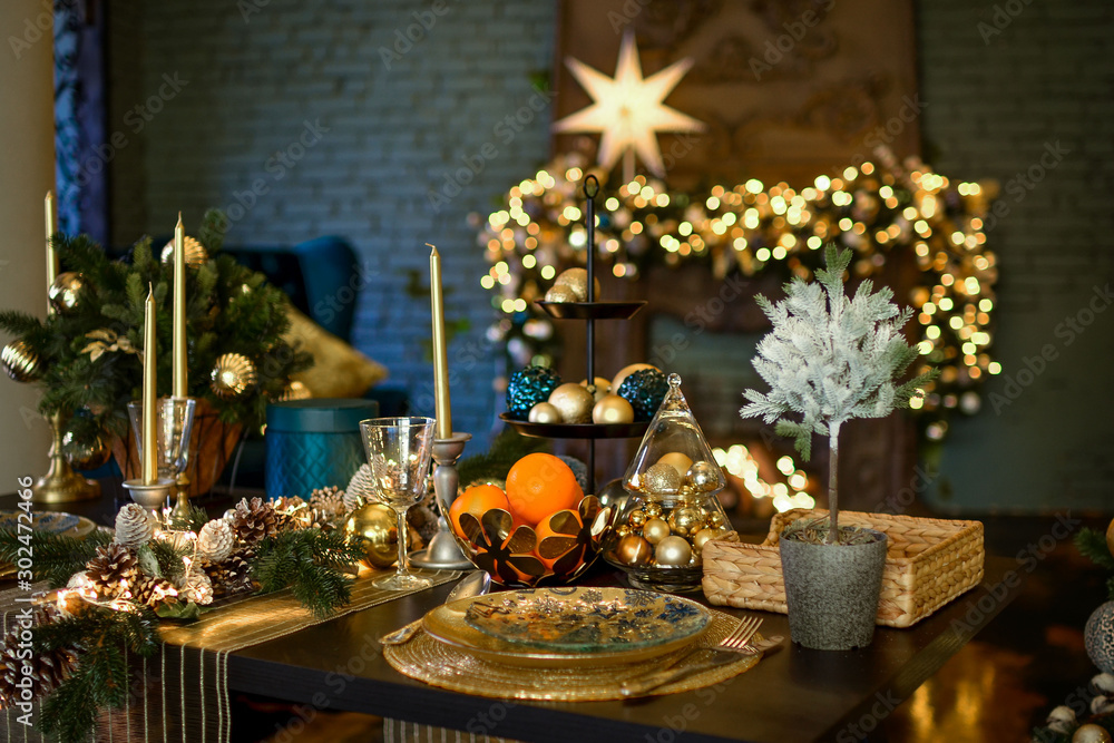A large table is decorated for the festive dinner and Christmas. Christmas, a big star glows brightly near the fireplace. Loft interior with fireplace decorated for Christmas. Evening photo in warm ti