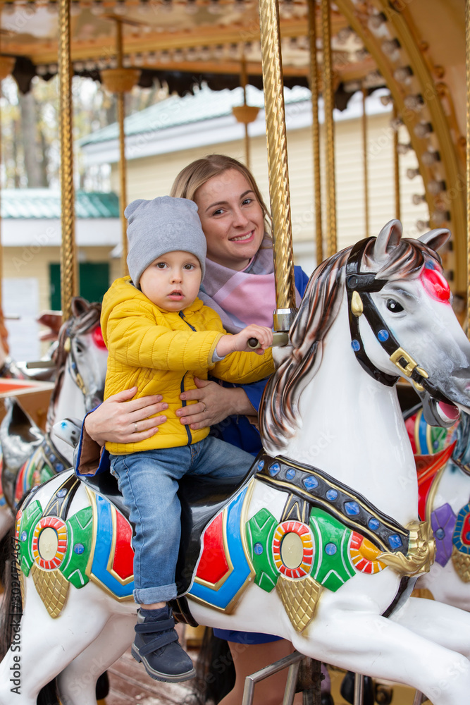 Mom with a cheerful baby on a carousel.Little son with mom in the park. Mom with a cheerful baby on a carousel.Little son with mom in the park.
