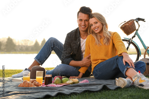 Happy young couple having picnic near lake on sunny day