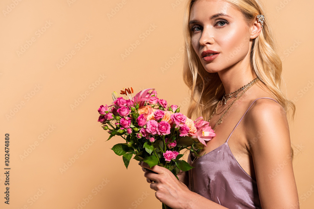 blonde woman in violet satin dress and necklace holding bouquet of flowers on beige blonde woman in violet satin dress and necklace holding bouquet of flowers on beige