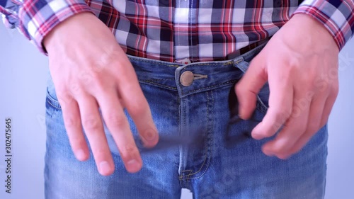Man unbuckled his belt and unbuttoned jeans by hands after having a heavy dinner. He pats his stomach. He is wearing jeans and plaid shirt, waist closeup. photo