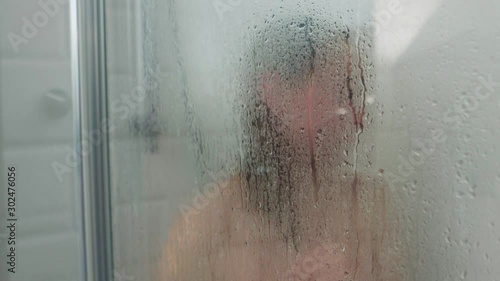 Unrecognizable woman washing body in shower cabin. Waterdrop on steamy glass.