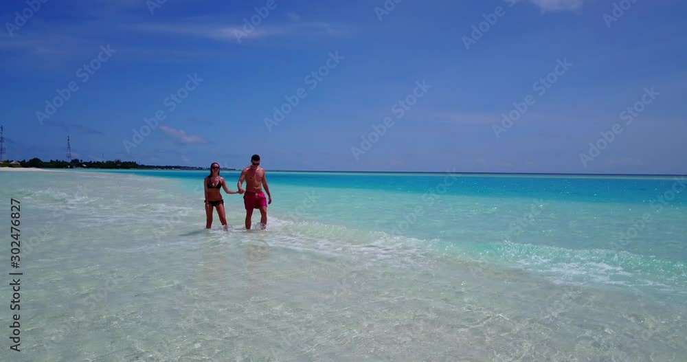 Happy couple walking across shallow sea water over white sandy stripe enjoying their vacations in Hawaii Happy couple walking across shallow sea water over white sandy stripe enjoying their vacations in Hawaii