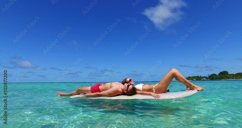 Young couple lying on surfboard floating over crystal vibrant water of lagoon surrounding tropical island in Thailand Young couple lying on surfboard floating over crystal vibrant water of lagoon surrounding tropical island in Thailand