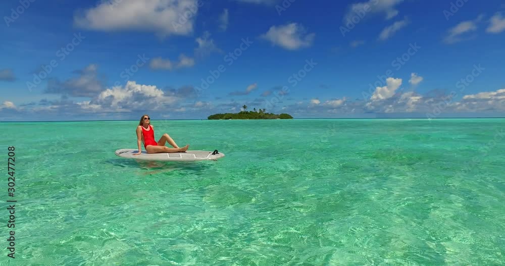 Beautiful girl in red swimsuit meditating on a surfboard floating over crystal emerald water of exotic bay in Maldives Beautiful girl in red swimsuit meditating on a surfboard floating over crystal emerald water of exotic bay in Maldives