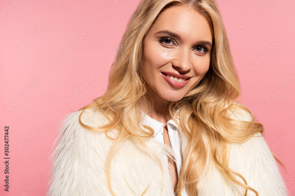 happy beautiful blonde woman in white faux fur jacket isolated on pink