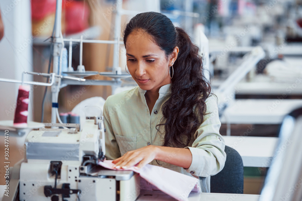 Dressmaker woman sews clothes on sewing machine in factory foto de Stock |  Adobe Stock