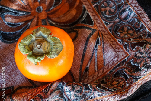 Bright orange persimmon, autumn symbol, on floral silk fabric background 