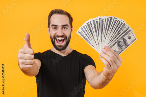 Image of unshaved man wearing t-shirt smiling and holding money cash