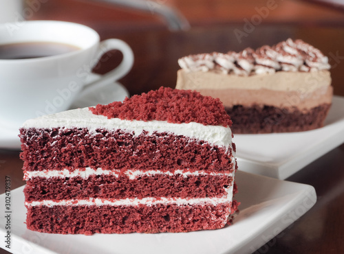 Slice of red velvet cake on a white plate. Close up of red velvet chocolate cake and tiramisu coffee cake with a cup of hot coffee on table.