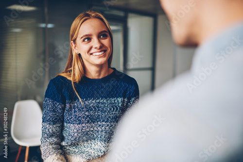 Young blonde woman smiling while answering questions during interview for getting job offer in office,happy female communicating with colleague during work break enjoying friendly atmosphere