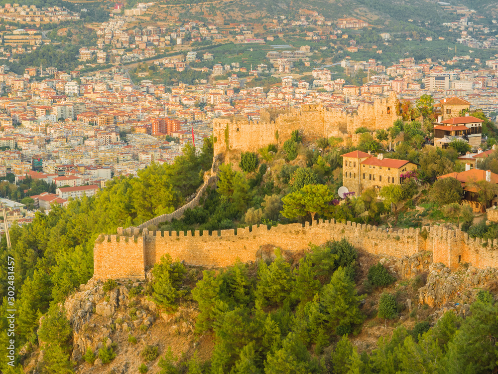 Alanya, Turkey. Beautiful view of the fortress Alanya Castle and the city of Alanya at sunset on a background of mountains. Vacation postcard background