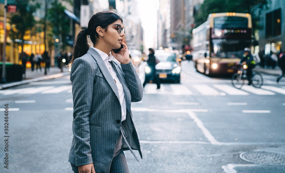 Side view of female lawyer formally dressed walking in financial district and making online cellphone conversation for consultancy with operator, woman proud ceo in spectacles calling to colleague