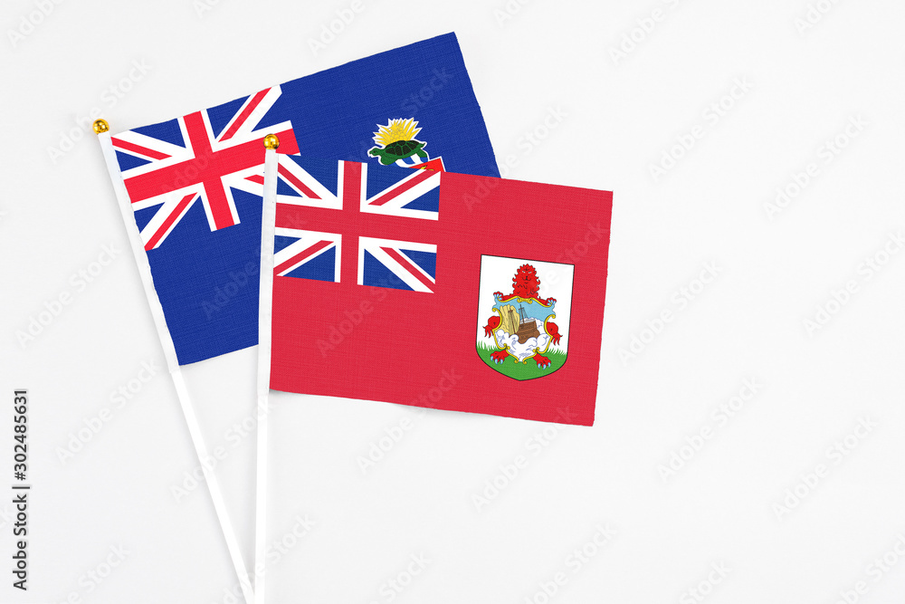 Bermuda and Cayman Islands stick flags on white background. High quality fabric, miniature national flag. Peaceful global concept.White floor for copy space.