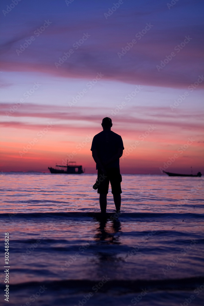 silhouette man standing alone seeing the beautiful colorful twilight sunset sky with orange pink purple at the seascape background.many fishing long tail boat chill and calm emotion cold mood & tone. silhouette man standing alone seeing the beautiful colorful twilight sunset sky with orange pink purple at the seascape background.many fishing long tail boat chill and calm emotion cold mood & tone.
