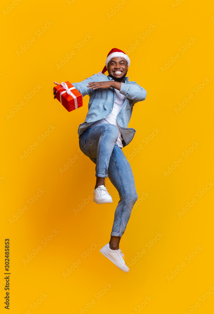 Positive black guy in Santa hat jumping with Xmas present Positive black guy in Santa hat jumping with Xmas present