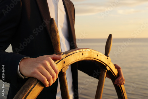 Businessman holding ship rudder and navigates in sunset light. photo