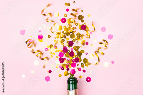Christmas composition with champagne bottle golden sparkles on pastel pink background. Holiday creative concept