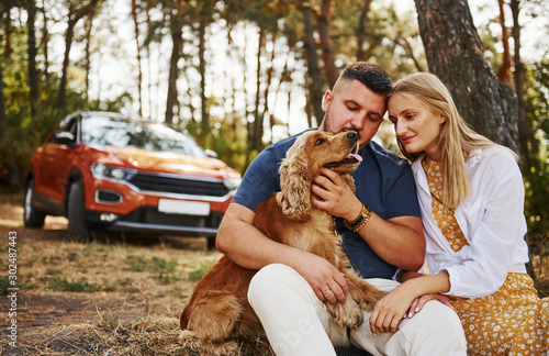 Couple with dog have weekend outdoors in the forest with car behind them