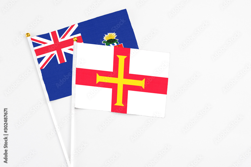 Guernsey and Cayman Islands stick flags on white background. High quality fabric, miniature national flag. Peaceful global concept.White floor for copy space.