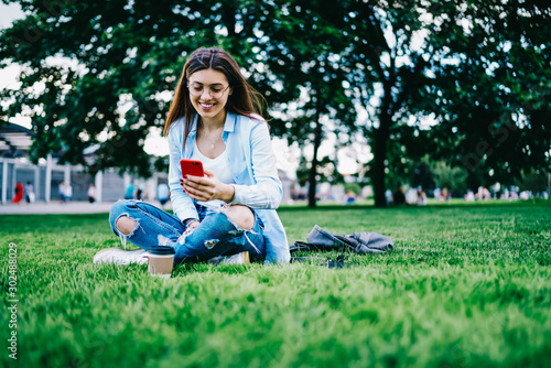 Smiling female happy about getting message from boyfriend on smartphone connected to 4G while resting in park, cheerful young woman checking likes social networks satisfied with online followers © BullRun
