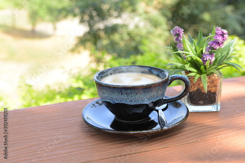 Hot coffee cup with spoon and small flowerpots put on wood table with blur background, refreshment on morning time, relaxing in the coffee shop.