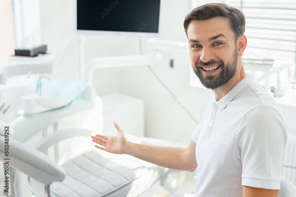 Smiling doctor sitting with folded arms in modern dental clinic