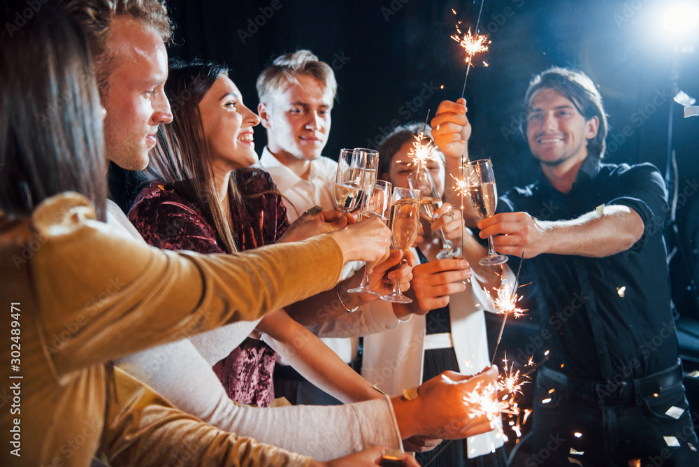 Fototapeta premium Knocking glasses. Group of cheerful friends celebrating new year indoors with drinks in hands
