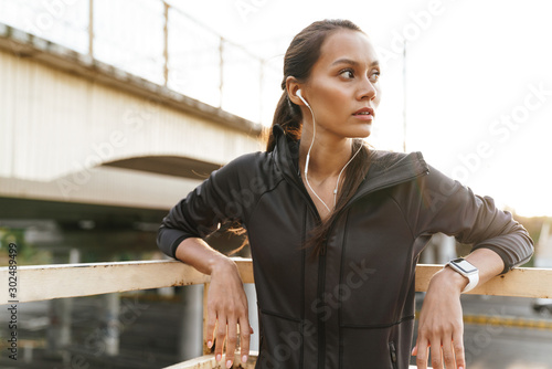 Image of young focused woman using earphones while leaning on railing © Drobot Dean