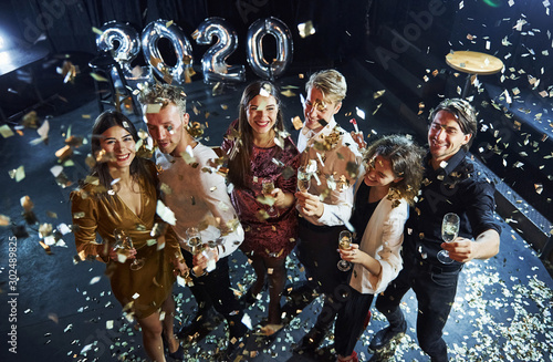 Confetti is in the air. Cheerful group of people with drinks in hands celebrating new 2020 year