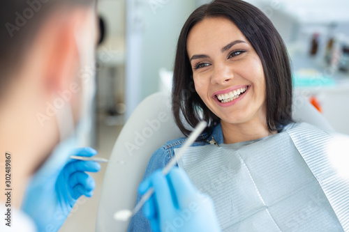 smiling woman in dental chair with doctor holding dental mirror