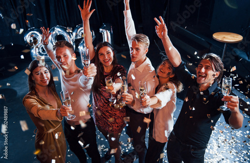 Cheerful group of people with drinks in hands celebrating new 2021 year