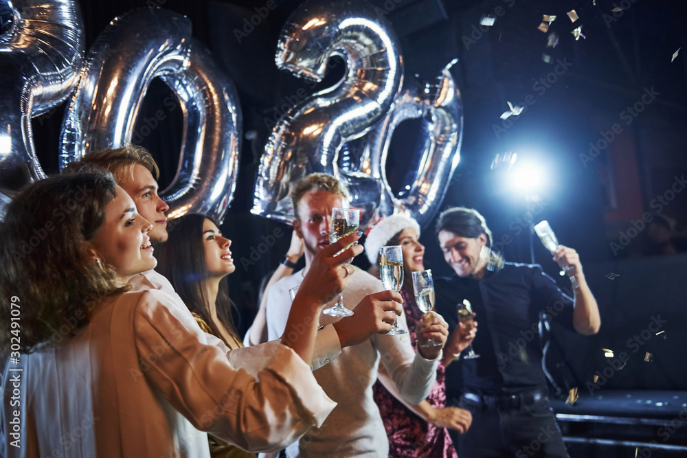 Cheerful group of people with drinks and balloons in hands celebrating new 2020 year
