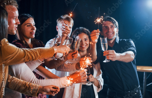 Group of cheerful friends celebrating new year indoors with drinks in hands