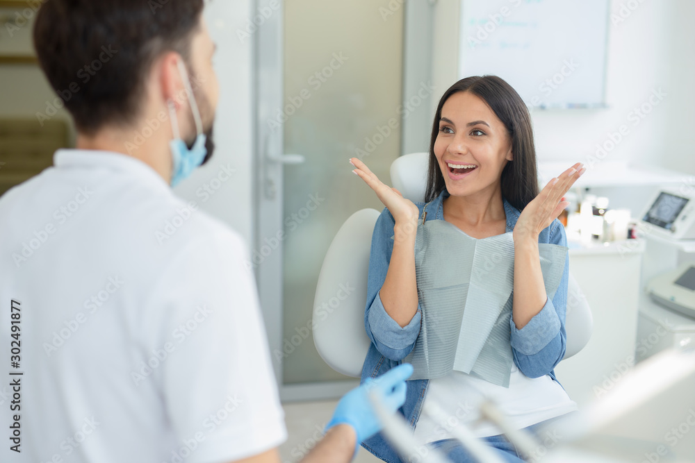 woman gesturing near dentist talking to her in clinic - obrazy, fototapety, plakaty 